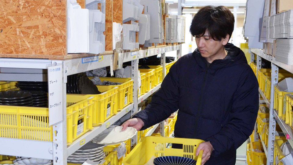 人気シリーズ「リンカ」を手に発送の準備をする伊藤祐輝専務＝土岐市下石町、カネコ小兵製陶所