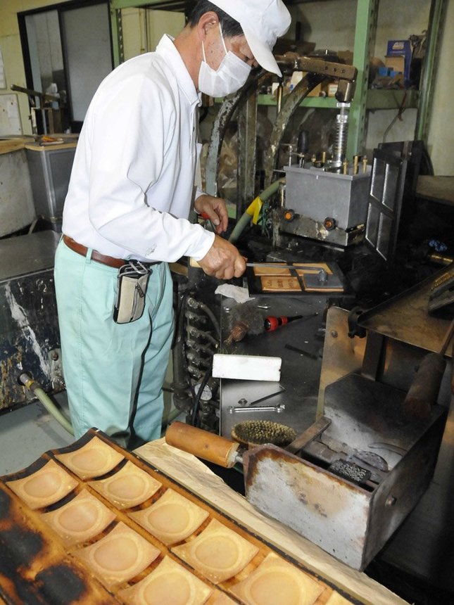 焼きたての瓦せんべいに図柄を刻印する稲垣伸作社長。反り板に素早く乗せ、特有の反りをつける