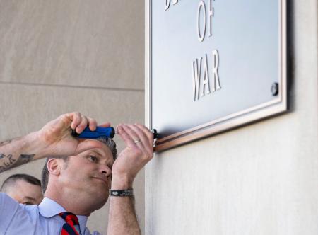 　米ワシントン近郊の国防総省入り口で、看板をかけ替えるヘグセス長官＝１３日（国防総省提供・共同）