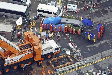 　下水道管内の捜索で発見された遺体を乗せ、陥没事故の現場を離れる車両（右上）＝２日、埼玉県八潮市