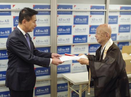 　前原誠司衆院議員（左）にルート見直しを求める署名を提出する京都仏教会の宮城泰年常務理事＝１３日午前、京都市