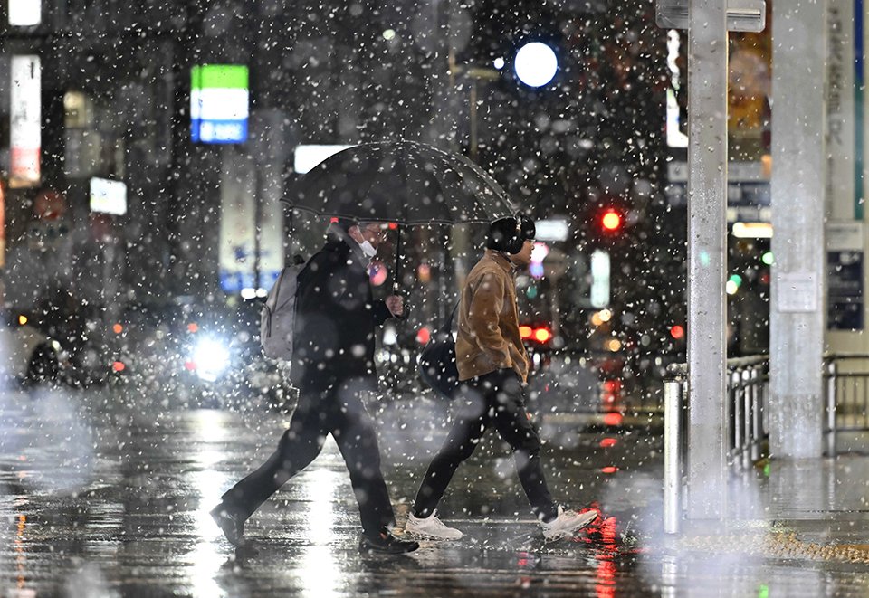 初雪が降る中、交差点を渡る人たち＝３日午後９時４１分、岐阜市神田町