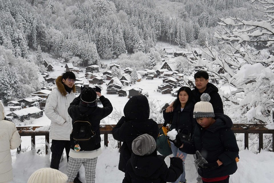 雪と記念撮影する観光客ら＝２１日午後０時２８分、大野郡白川村荻町、荻町城跡展望台