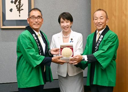 　静岡県温室農業協同組合クラウンメロン支所の沢木勝支所長（左）らから「クラウンメロン」を受け取る高市首相（中央）＝８日午後、首相官邸（山本裕三事務所提供）