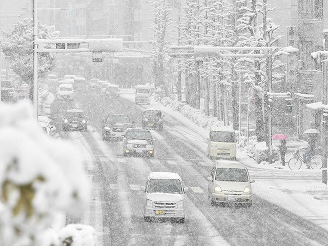 雪が降る中、金華橋通りをスピードを落として走る車＝１８日午前８時３４分、岐阜市内