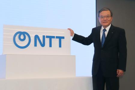 　「ＮＴＴ」への社名変更に伴う式典で、ロゴと写真に納まる島田明社長＝１日午前、東京都内