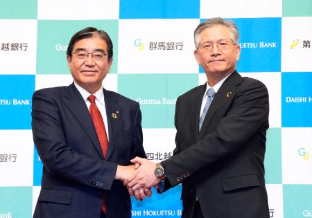 　記者会見を終え握手する群馬銀行の深井彰彦頭取（左）と第四北越ＦＧの殖栗道郎社長＝２４日午後、東京都内