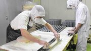 餅つき機で仕上げた生地を、あられの型に入れて成型する作業員