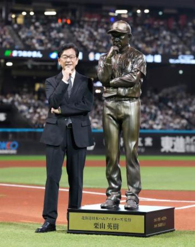 　野球殿堂入りを記念したセレモニーで、自らの立像の横で写真に納まる日本ハム前監督の栗山英樹さん＝エスコンフィールド