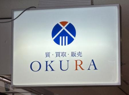 　高級腕時計の中古品販売を手がける「ＯＫＵＲＡ」の看板＝２３日午後、福岡市中央区