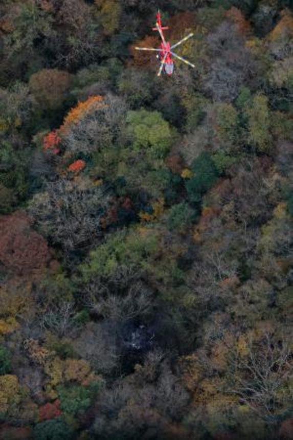 　小型機が墜落したとみられる現場（下）で救助活動を行う消防ヘリ＝１８日午後１時５分、福岡県八女市（共同通信社ヘリから）