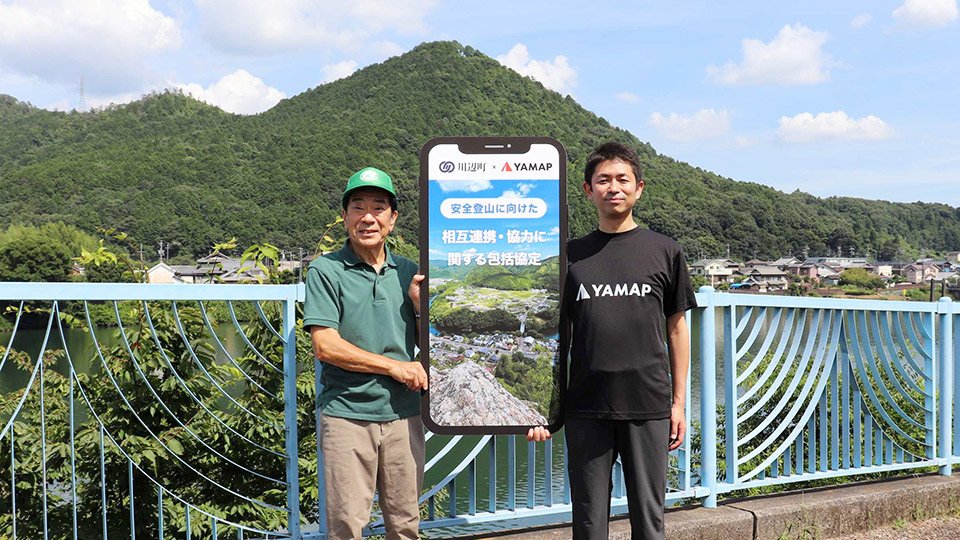 包括協定を結んだ佐藤光宏町長（左）と小野寺洋本部長。後方の山は愛宕山＝川辺町中川辺