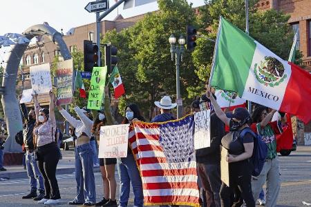 　米国やメキシコの国旗を掲げ、移民取り締まりに抗議する人々＝８日、ロサンゼルス