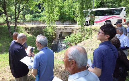 　メチル水銀を含む汚染された水を流した排水口（奥）を視察するイタイイタイ病の被害者団体の関係者ら＝２１日午後、新潟県阿賀町