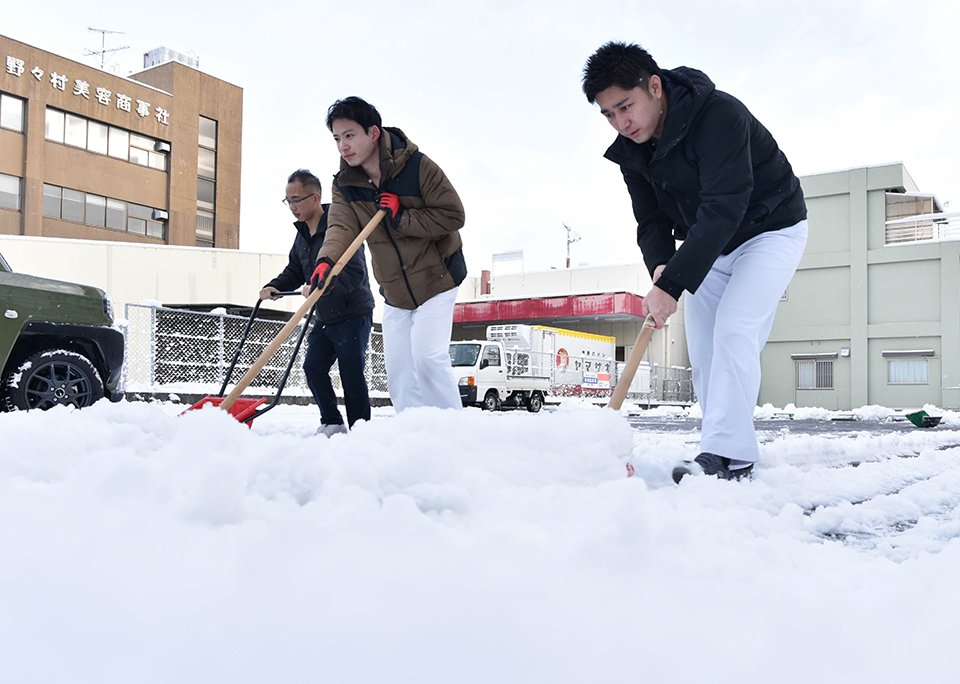 雪の舞う中、朝から駐車場の雪かきに追われる人たち＝２３日午前８時１７分、岐阜市島栄町