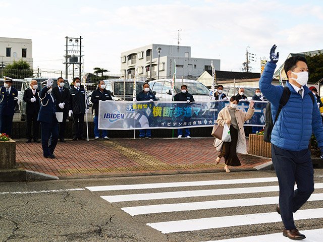 横断幕を手にし、通勤する社員に手を上げて渡るよう呼び掛ける参加者たち＝大垣市神田町
