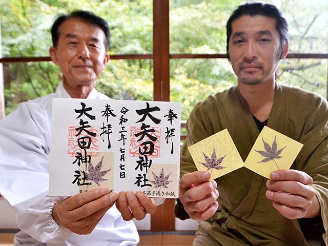 モミジ葉入りで直筆の御朱印を手にする眞清辰也宮司（左）とシール加工したモミジ葉入りの和紙を手にする千田崇統さん＝美濃市大矢田、大矢田神社