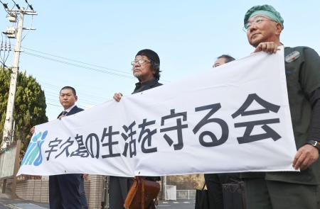 　仮処分の申し立て後、長崎地裁佐世保支部前で横断幕を掲げるＮＰＯ法人「宇久島の生活を守る会」の佐々木浄栄会長（左端）ら＝１９日午後、佐世保市