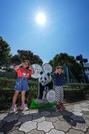 　強い日差しの中、アドベンチャーワールドのジャイアントパンダ楓浜のパネルと記念写真に納まるきょうだい＝２７日午前、和歌山県白浜町