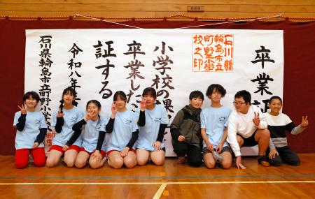 　大きな紙でできた「卒業証書」の前で、記念写真に納まる川原脩伸さん（右端）ら＝２１日午後、石川県輪島市の町野小