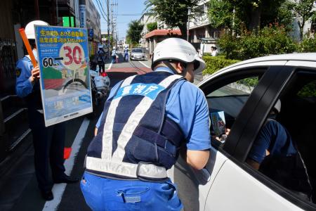 　ドライバーに生活道路の法定速度引き下げを周知する警視庁の警察官＝２５日、東京都世田谷区