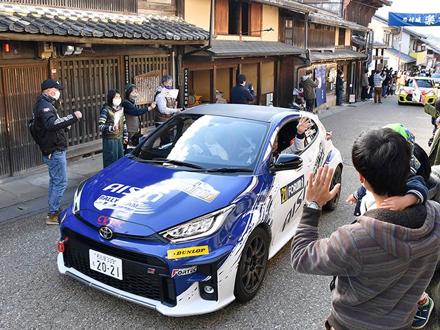 岩村本通りを走り抜けるラリーカー。沿道の観光客らが手や旗を振って迎えた＝１４日午後、恵那市岩村町