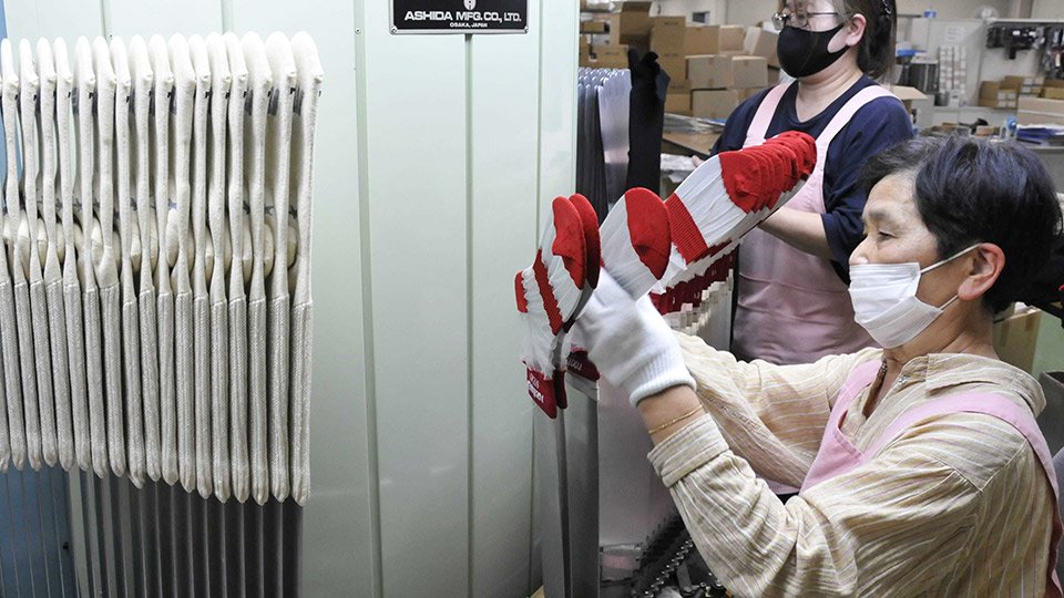 蒸気を当てて成型する機械に編み上げた靴下をセットしていく従業員