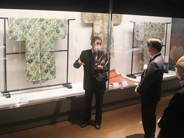 開幕した特別展「近世能装束の世界　用の美」で山口憲さん（左）の解説を聞く来場者＝１７日午前９時４９分、岐阜市大宮町、市歴史博物館