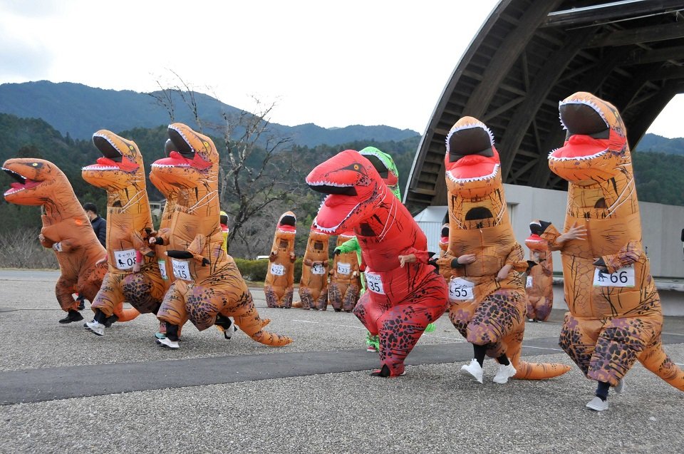 号砲とともに、ティラノサウルスの着ぐるみを大きく揺らしながら勢いよく飛び出す参加者＝中津川市付知町、道の駅「花街道付知」イベント広場