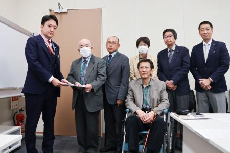 　警察庁の担当者に要請文を手渡す「犯罪被害補償を求める会」の藤本護代表理事（左から２人目）＝２９日午前、国会
