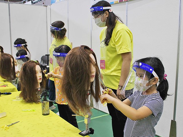 美容師ブースでマネキンのヘアカットを体験する子どもら＝岐阜市薮田南、ＯＫＢぎふ清流アリーナ