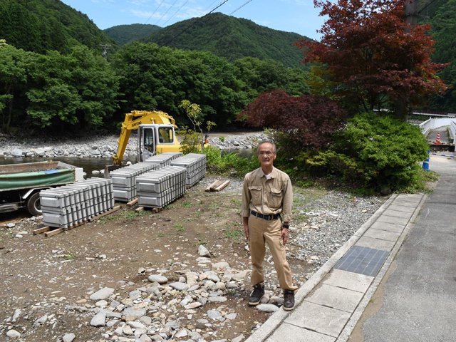 自宅玄関があった場所に立つ桐谷猛さん。自宅跡では護岸工事が進む＝１日午前、下呂市小坂町門坂