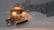 しぶきを上げながら雪を道路脇に飛ばす除雪ブルドーザー