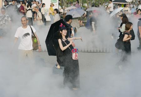 　強い日差しの中、大阪・関西万博会場で日傘を差しミストを浴びる来場者＝２７日、大阪市此花区の夢洲