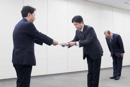 　総務省の担当者から行政指導の文書を受け取るＫＤＤＩの松田浩路社長（中央）＝２９日午後、東京都千代田区