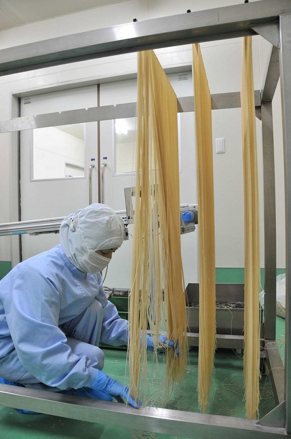 製麺された米粉パスタをラックにかける従業員